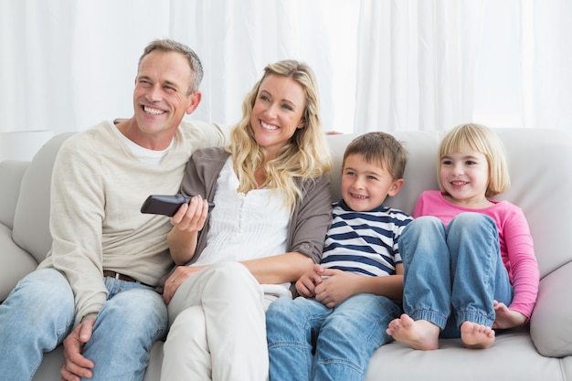 Família sorridente sentada no sofá mudando o canal de TV