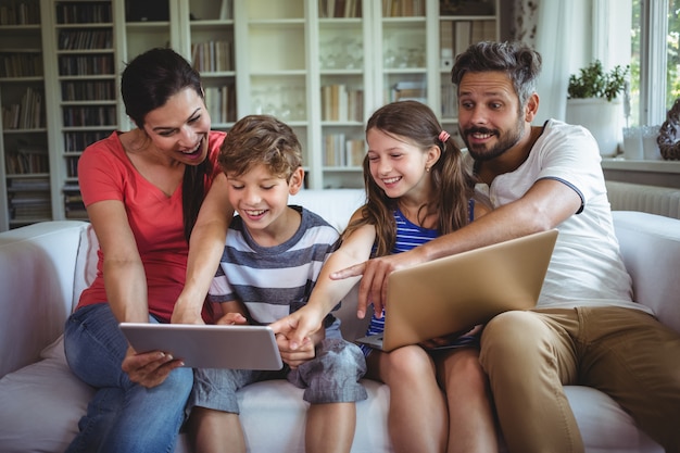 Família sorridente, sentado no sofá e apontando para tablet digital