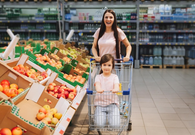 Familia en el supermercado joven madre y su pequeña hija sonríen y compran comida Concepto de comida saludable mamá e hija compran verduras y frutas en el supermercado