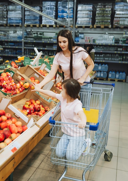 Familia en el supermercado joven madre y su pequeña hija sonríen y compran comida Concepto de comida saludable mamá e hija compran verduras y frutas en el supermercado