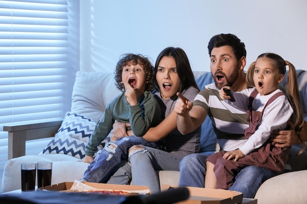 Família surpreendida assistindo TV com pizza no sofá em casa