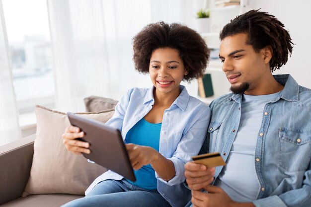 família, tecnologia, compras on-line e conceito de pessoas - casal feliz sorridente com computador tablet pc e cartão de crédito em casa