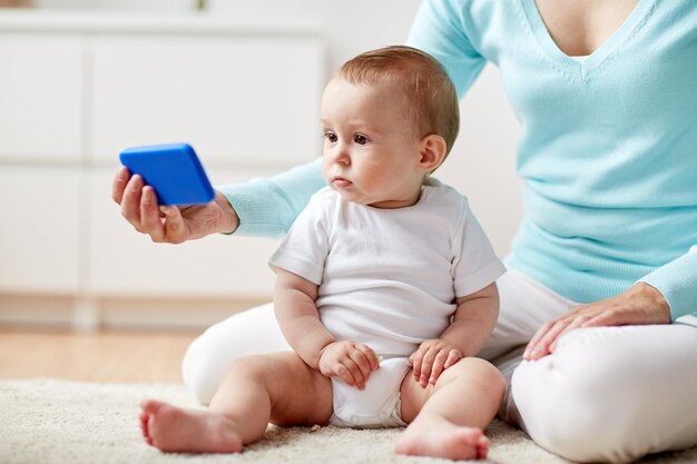 família, tecnologia, criança e conceito de paternidade - close-up da jovem mãe mostrando smartphone para bebê em casa