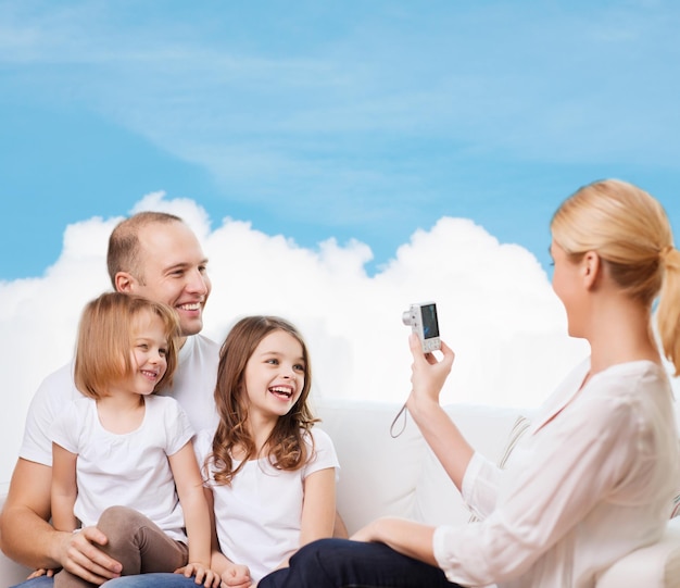 familia, tecnología y gente - madre, padre y niñas sonrientes con cámara sobre cielo azul y fondo de nube blanca