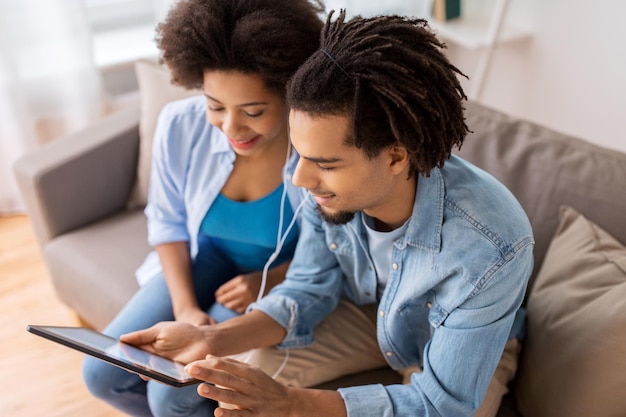 família, tecnologia, internet e conceito de pessoas - casal feliz com computador tablet pc e fones de ouvido ouvindo música em casa