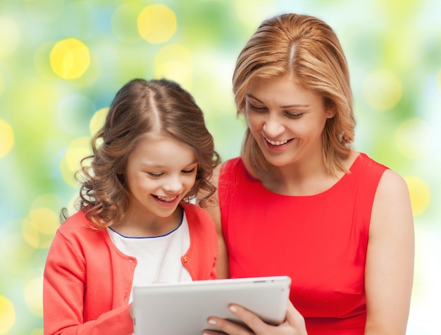 família, tecnologia, pessoas e conceito de férias de natal - mãe e filha felizes com computador tablet pc sobre fundo de luzes verdes