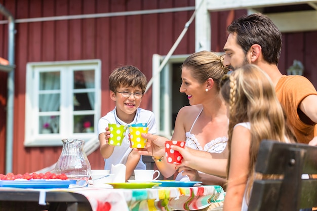 Foto familia tomando café y comiendo pastel frente a casa