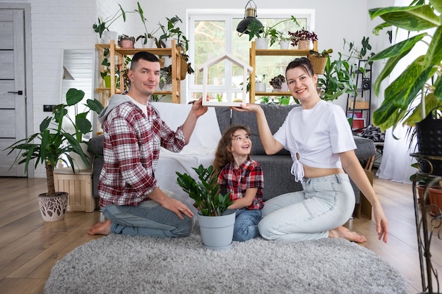 Foto família tradicional com criança está aproveitando a nova casa sentada no sofá e segurando o telhado seguro hipotecário e proteção comprando e mudando para sua própria casa verde com vaso de plantas