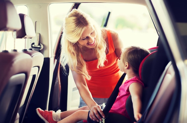 Família, transporte, segurança, viagem e conceito de pessoas - mãe feliz prendendo criança com cinto de segurança