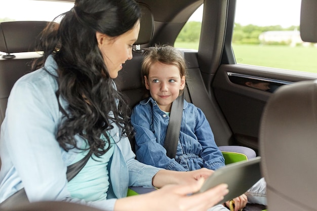 família, transporte, viagem, viagens e conceito de pessoas - mulher feliz e filha pequena com computador tablet pc dirigindo no carro
