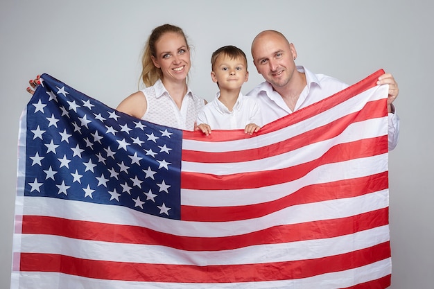 Una familia de tres con una bandera estadounidense sobre un fondo blanco.