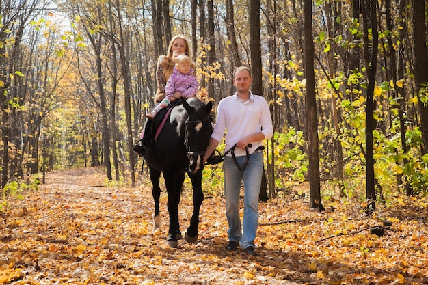 Familia de tres con un caballo a pasear por el bosque de otoño