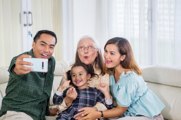 La familia de tres generaciones sonrientes se toma selfie en casa