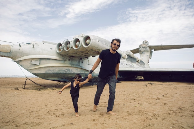 Família, um menino e seu pai em roupas de roqueiro estão em um avião ekranoplan abandonado à beira-mar no Daguestão