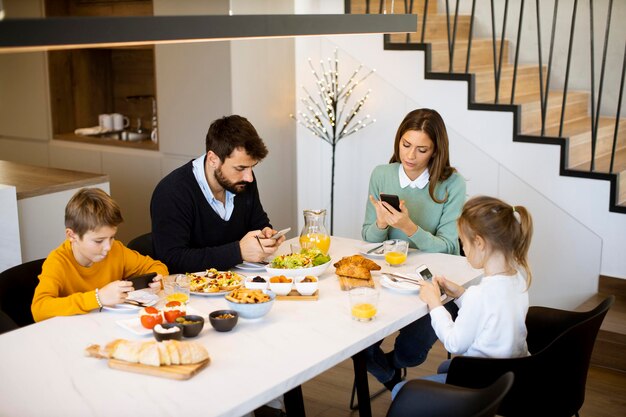 Família jovem e elegante com dois filhos preparando um café da manhã  vegetariano saudável com legumes frescos na cozinha