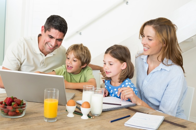 Familia usando una computadora portátil mientras toma el desayuno