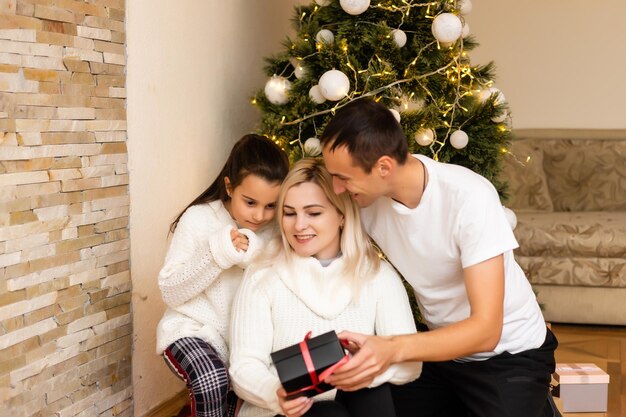 Familia, vacaciones y gente - madre sonriente, padre y niña sobre fondo de luces de árbol de Navidad