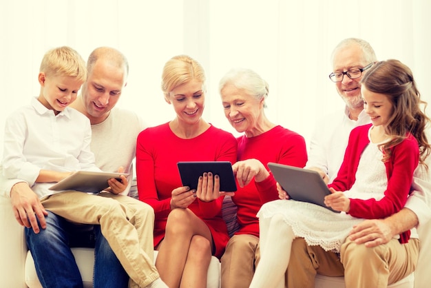 familia, vacaciones, navidad, tecnología y concepto de personas - familia sonriente con computadoras tablet pc sentadas en el sofá en casa