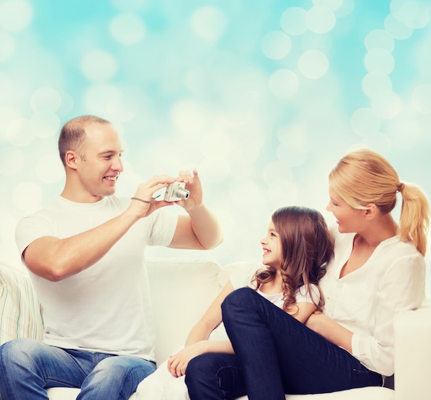 familia, vacaciones, tecnología y gente - madre, padre y niña sonrientes con cámara sobre fondo de luces azules