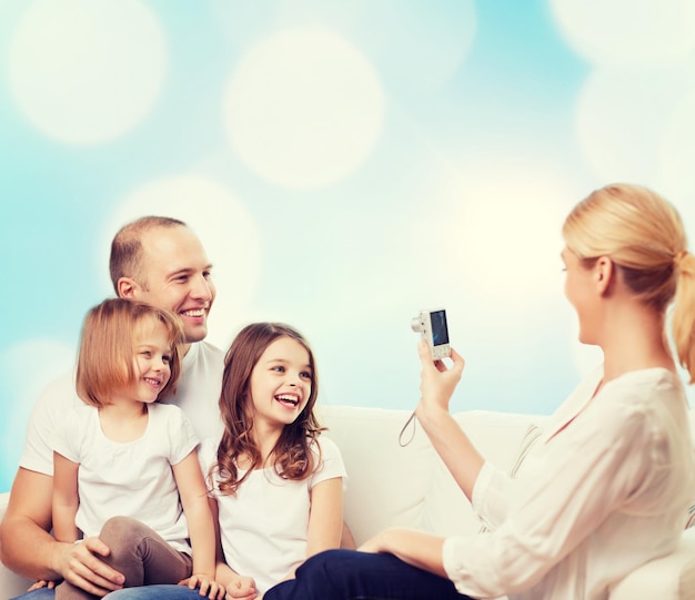 familia, vacaciones, tecnología y gente - madre, padre y niñas sonrientes con cámara sobre fondo de luces azules