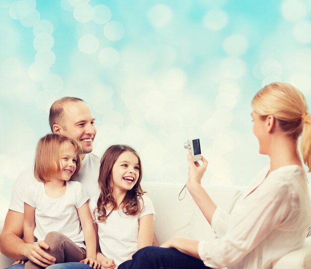 familia, vacaciones, tecnología y gente - madre, padre y niñas sonrientes con cámara sobre fondo de luces azules