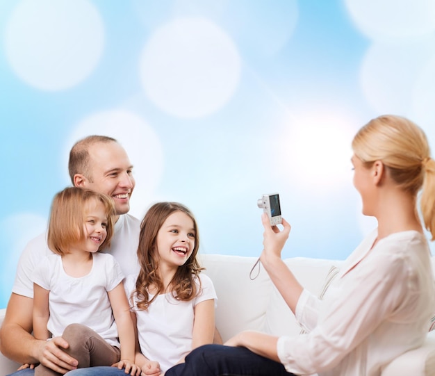 familia, vacaciones, tecnología y gente - madre, padre y niñas sonrientes con cámara sobre fondo de luces azules