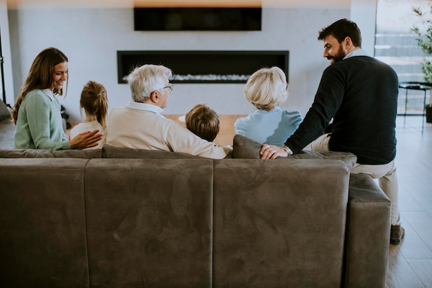 Familia de varias generaciones sentados juntos en el sofá del apartamento moderno y viendo la televisión