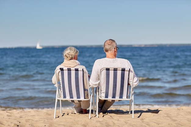 família, velhice, viagens, turismo e conceito de pessoas - feliz casal sênior sentado em espreguiçadeiras na praia de verão