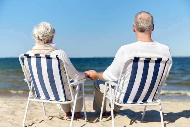 família, velhice, viagens, turismo e conceito de pessoas - feliz casal sênior sentado em espreguiçadeiras na praia de verão