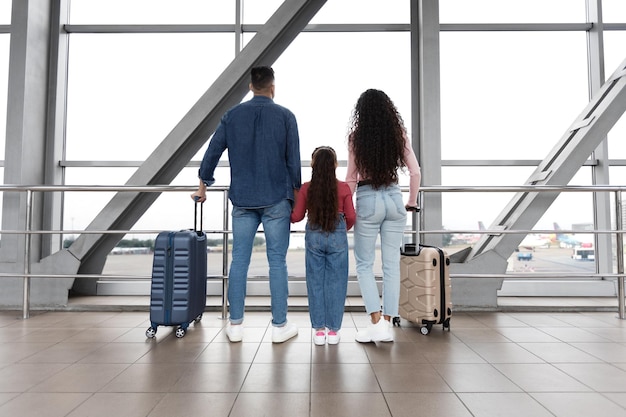 Familia de viajes aéreos en el aeropuerto tomados de la mano y mirando la ventana