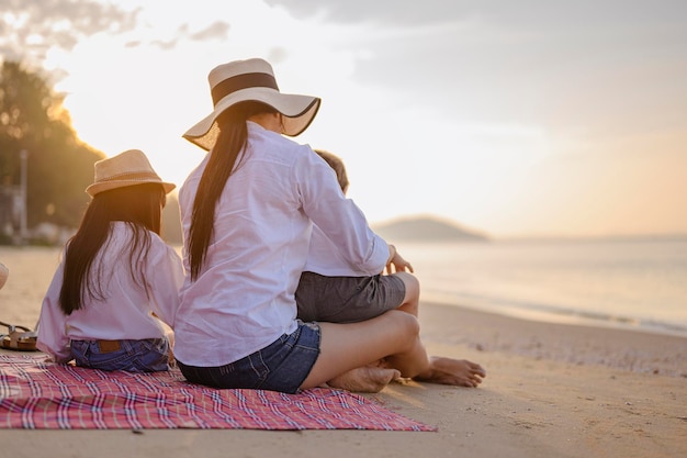 Familia, viajes, playa, relax, estilo de vida, concepto de vacaciones. Padres e hijos que disfrutan de un picnic en la playa al atardecer en vacaciones.