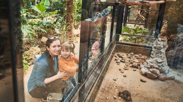 La familia en el zoológico mira a los animales a través de un vidrio de seguridad.