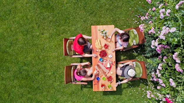 Familiares y amigos comiendo juntos al aire libre en la fiesta en el jardín de verano. Vista aérea de mesa con comida y bebida desde arriba. Concepto de ocio, vacaciones y picnic.