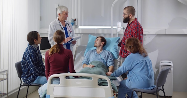 Familiares y amigos visitando al paciente en la sala del hospital y hablando con el médico