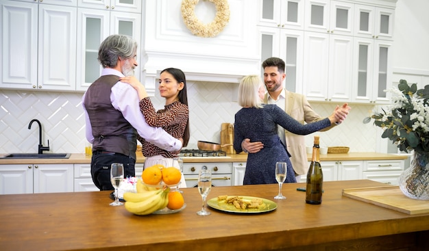 Familiares felices bailando durante la celebración de cumpleaños en la cocina cerca de la mesa