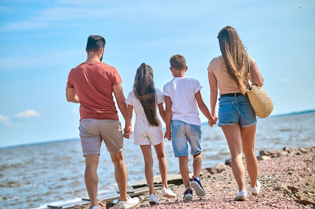 Familie am Strand. Eine Familie, die Händchen haltend an einem Ufer spazieren geht