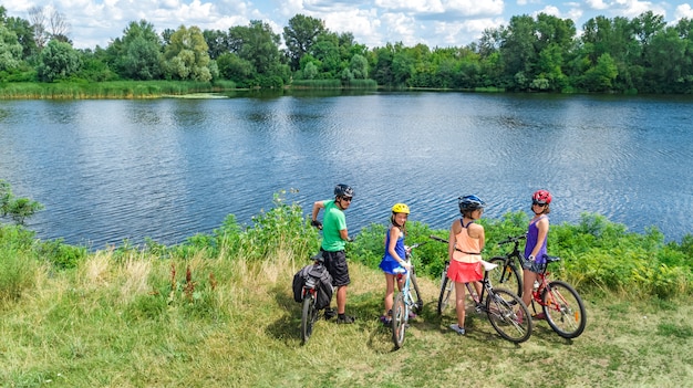 Familie auf den Fahrrädern, die draußen, aktive Eltern und Kinder auf Fahrrädern, Luftdraufsicht der glücklichen Familie mit den Kindern sich entspannen nahe schönem Fluss von oben, Sport und Eignungskonzept radfahren