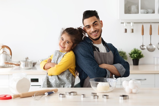 Familie backen. Glücklicher arabischer Vater und Tochter in Schürzen, die in der Küche posieren