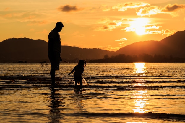 Familie, die am Strand in der Sonnenuntergangzeit spielt