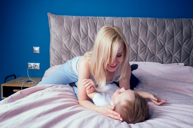 Familie, die am Wochenende zusammen Spaß hat. Mutter und zwei Kinder im Bett. blonde mutter und baby jungen spielen morgens im schlafzimmer. Eltern und Kleinkind entspannen sich zu Hause. Muttertag