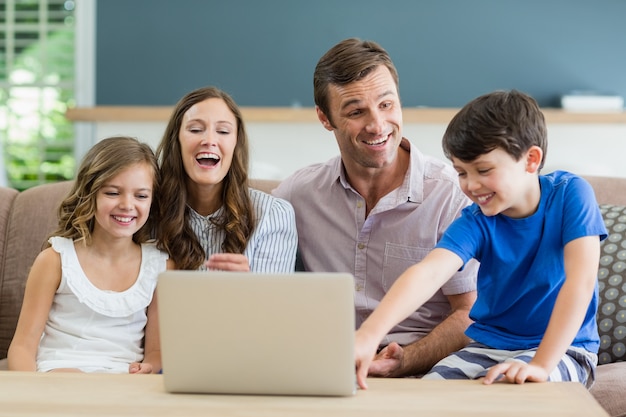 Familie, die auf Sofa mit Laptop im Wohnzimmer zu Hause sitzt