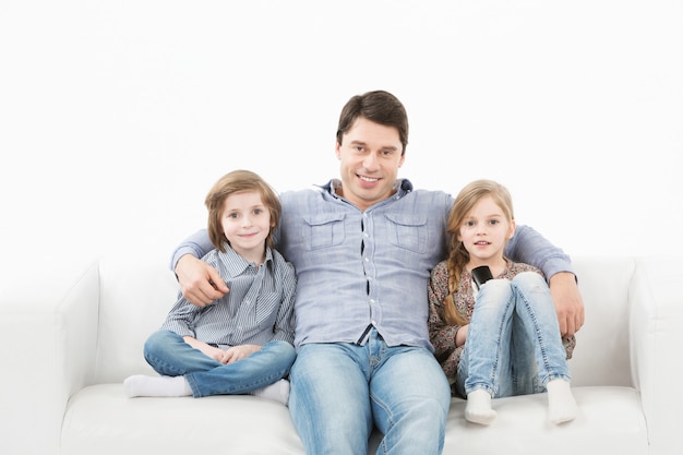 Familie, die auf Sofa sitzt, der Kamera auf weißer Wand lächelt