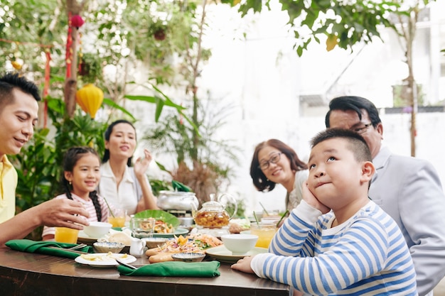 Familie, die einen entzückenden nachdenklichen kleinen Jungen ansieht, der am Esstisch sitzt