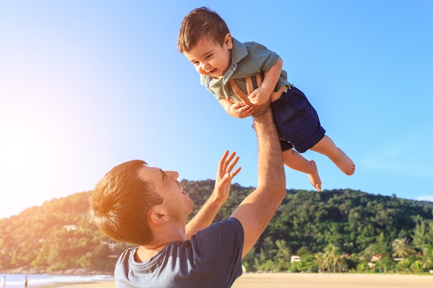 Familie, die mit dem Sohn auf dem Strand zur Sonnenuntergangzeit spielt