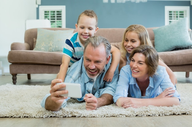 Familie, die selfie nimmt, während sie zusammen auf dem Teppich liegen