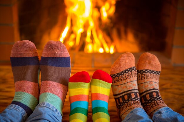 Familie, die sich zu Hause entspannt. Füße in Weihnachtssocken in der Nähe von Kamin. Winterurlaubskonzept