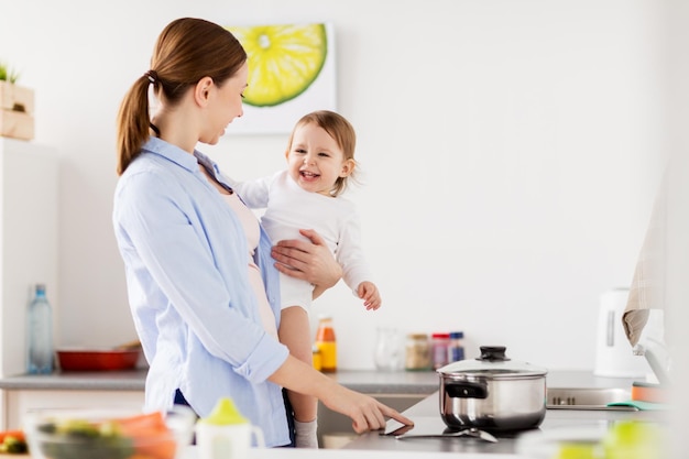 Familie, Essen, gesunde Ernährung und Menschenkonzept - glückliche Mutter und kleines Mädchen kochen gemeinsam Abendessen in der heimischen Küche