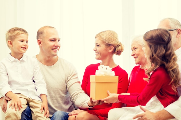 familie, feiertage, generation, weihnachten und personenkonzept - lächelnde familie mit geschenkbox, die zu hause auf der couch sitzt