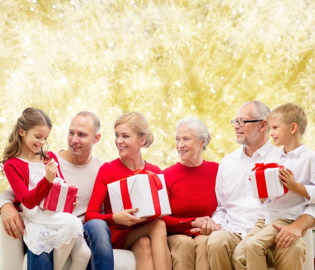 familie, feiertage, generation, weihnachten und personenkonzept - lächelnde familie mit geschenkboxen, die auf couch über gelbem lichthintergrund sitzen