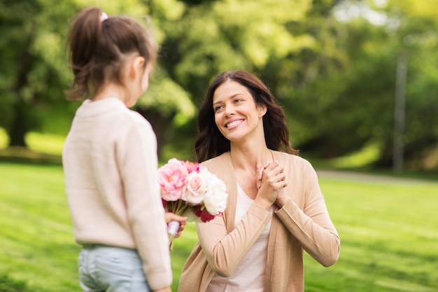 Familie, Feiertage und Menschen Konzept - glückliches kleines Mädchen gibt seiner Mutter Blumen im Sommerpark